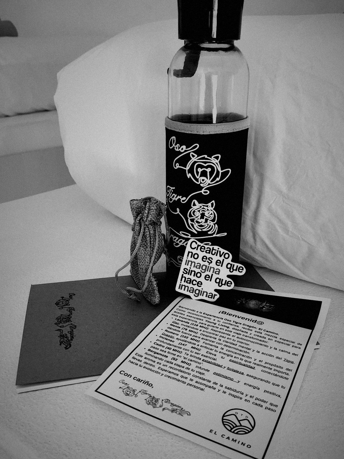 El kit de bienvenida de El Camino sobre la cama: botella, libreta, bolsita y carta