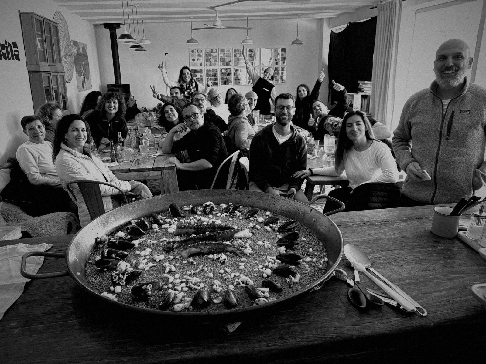 El grupo alrededor de una mesa larga, celebrando ante una gran paella