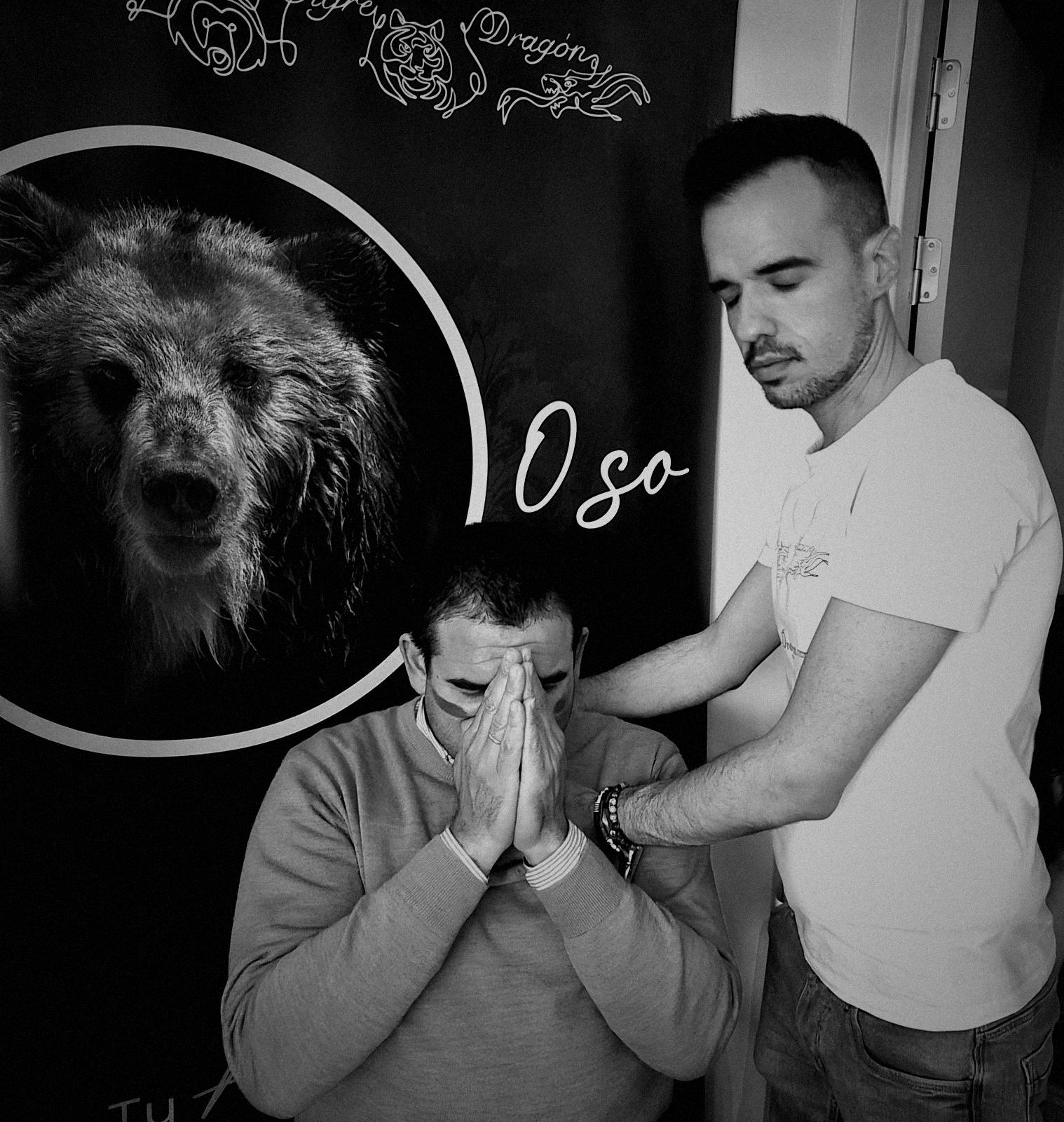 Un facilitador acompaña con las manos a un participante que se cubre el rostro, ante el roll-up del oso